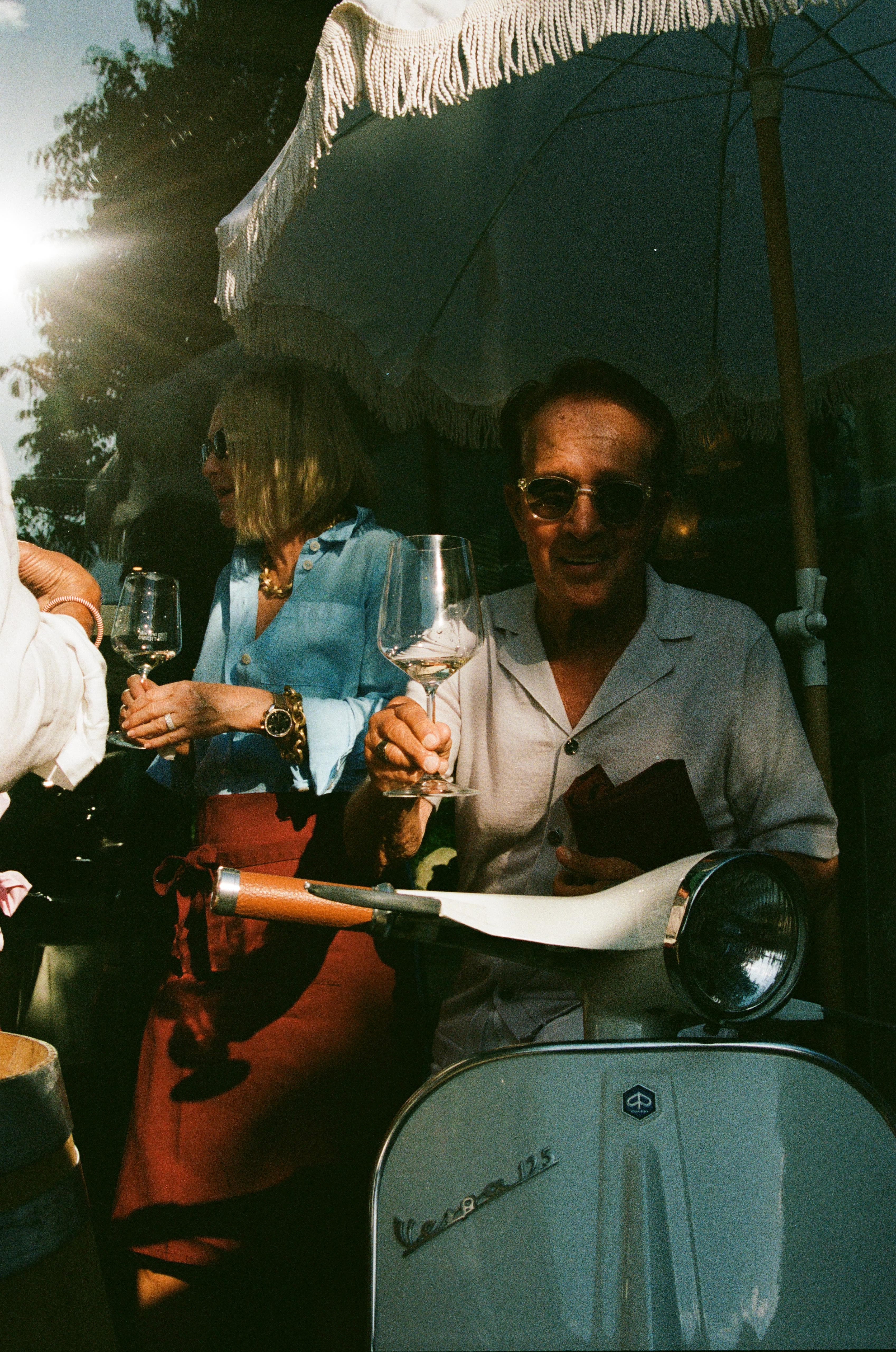 Ospiti con calici di vino accanto alla Vespa 125 d'epoca all'aperitivo