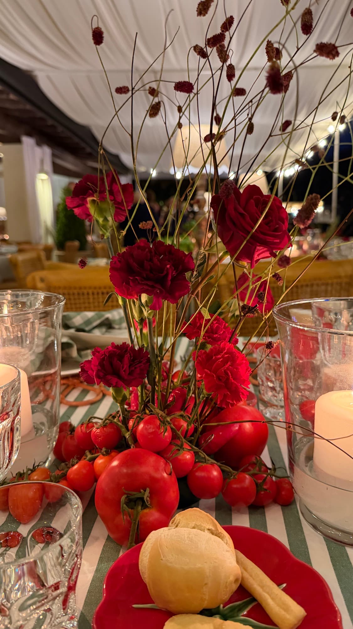 Centrotavola con rose rosse, pomodorini e candele su tovaglia a righe